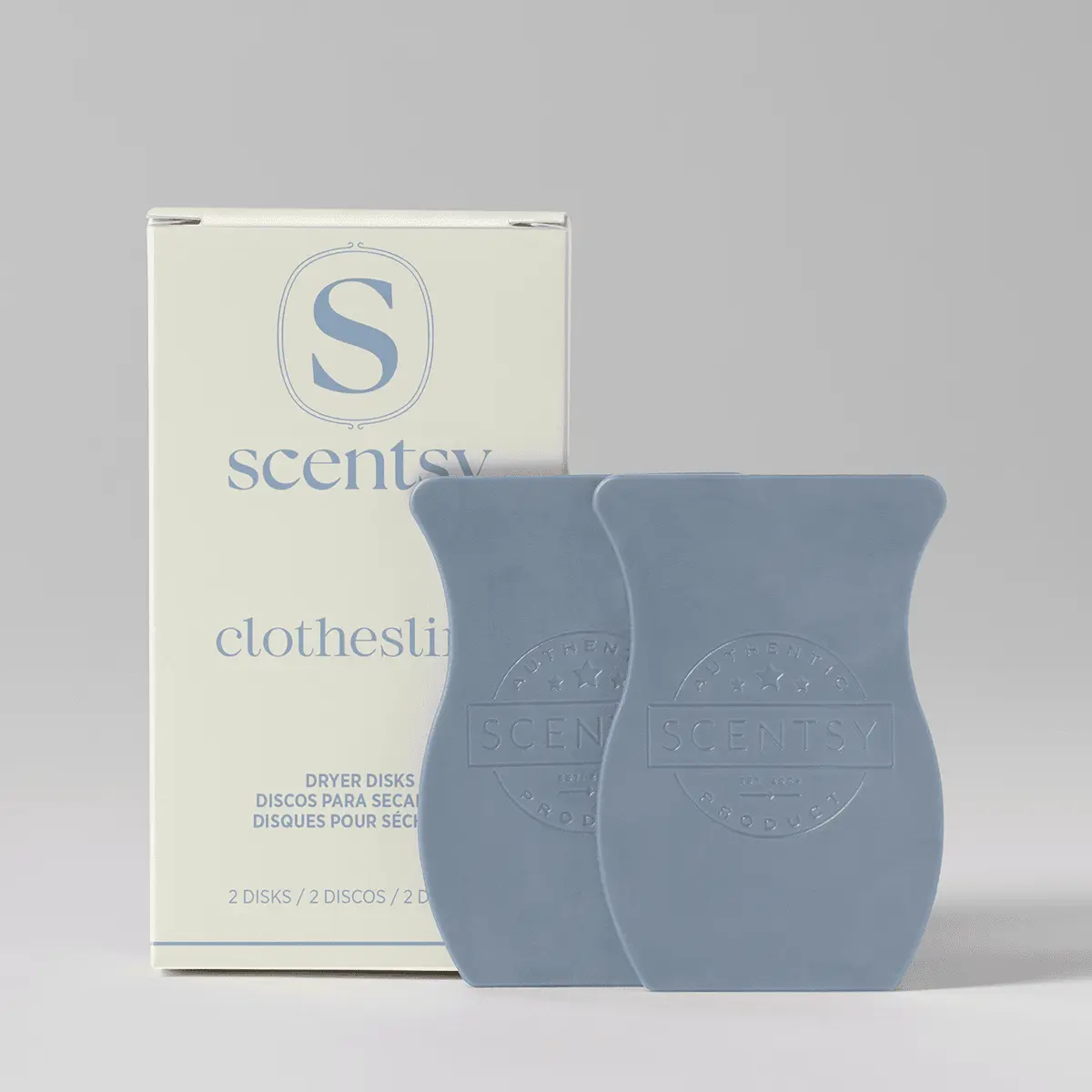 Two slate-blue waffle-textured dryer disks with embossed Scentsy branding, displayed next to cream packaging labelled Clothesline Dryer Disks