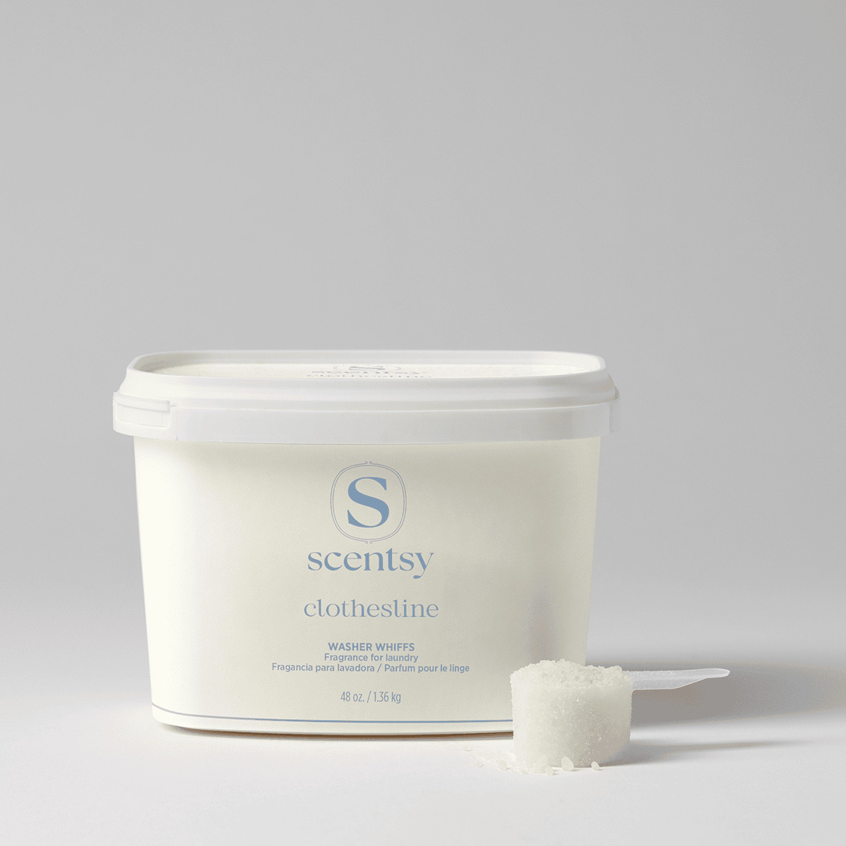 Cream-coloured tub of Scentsy Clothesline Washer Whiffs Tub with white lid and a measuring scoop filled with white granules beside it