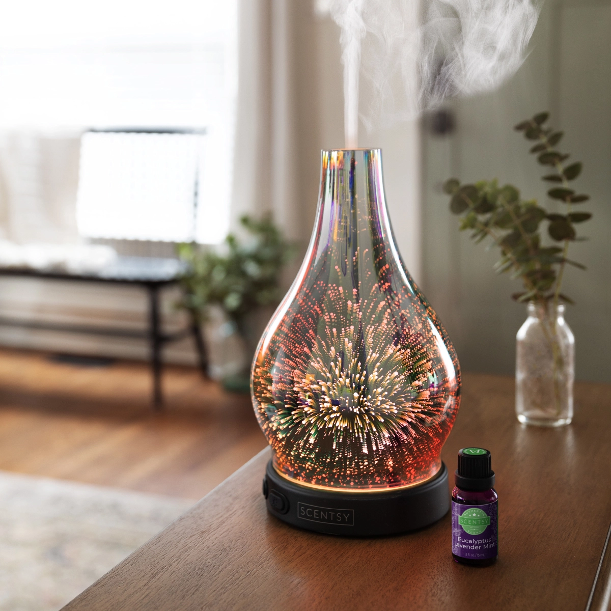 Glass diffuser with a teardrop shape and dimensional starburst light pattern in amber and gold tones, the Stargaze Scentsy Diffuser, on a black base with mist rising from the top