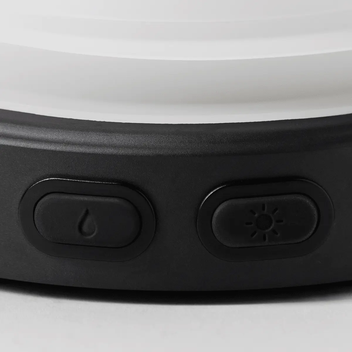 Curved ceramic diffuser with a white glossy top and textured black base, featuring two oval control buttons with power and brightness icons