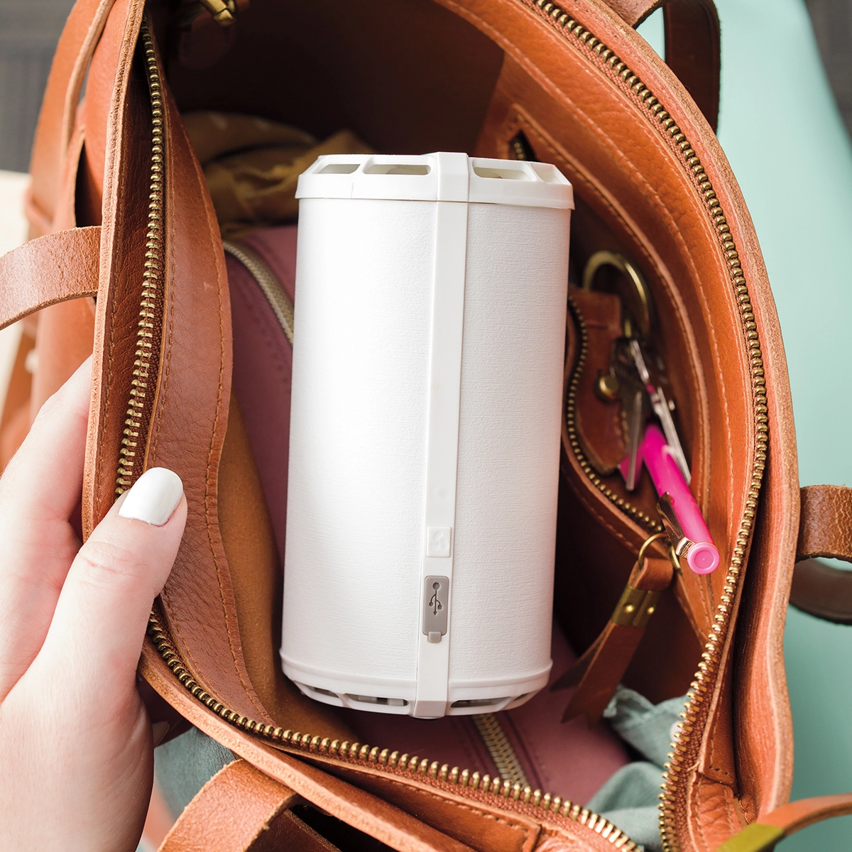 Compact white cylindrical Scentsy Air Go+ diffuser held inside an open tan leather handbag