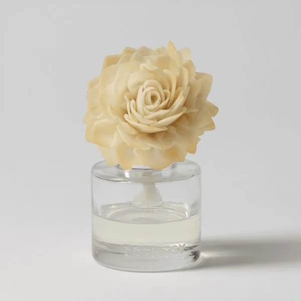 Cream-coloured rose-shaped wax flower with layered petals sitting atop a clear glass diffuser filled with pale liquid, the Go, Go, Mango - Dahlia Darling Fragrance Flower