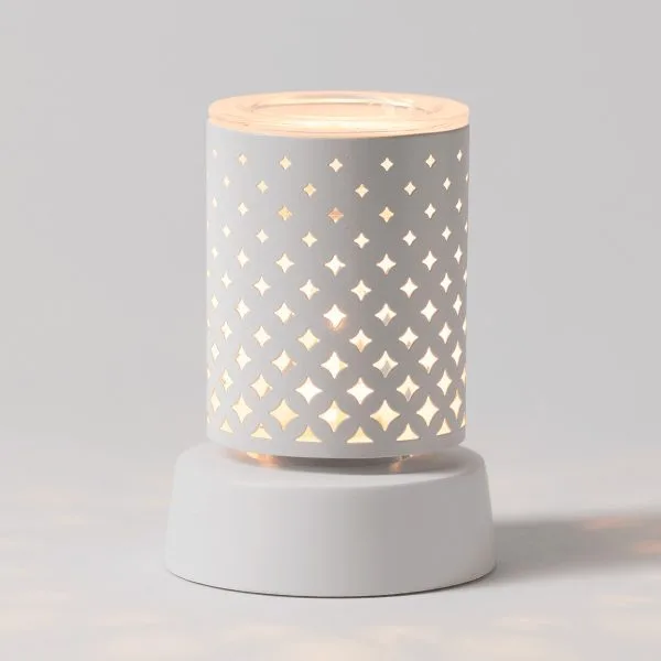 White cylindrical ceramic warmer with a repeating four-pointed star cutout pattern that glows warmly when lit, sitting on a matching white cylindrical tabletop base, the Light From Within Mini Scentsy Warmer with Tabletop Base