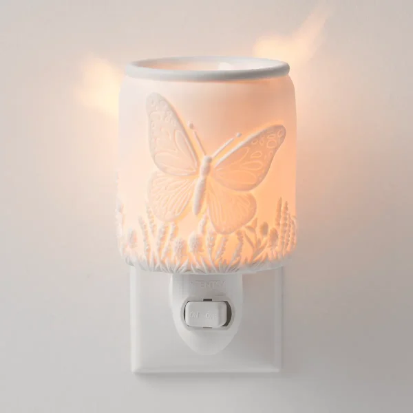 White plug-in warmer with embossed butterfly and grass design, lit to show warm amber glow, the Butterfly Season Mini Scentsy Warmer