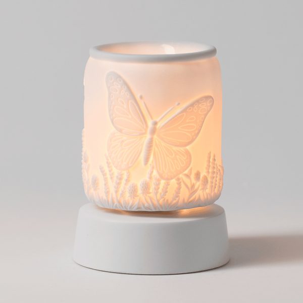 Ceramic warmer glowing warm white with an embossed butterfly and wildflower design, the Butterfly Season Mini Scentsy Warmer with Tabletop Base, mounted on a round white ceramic base