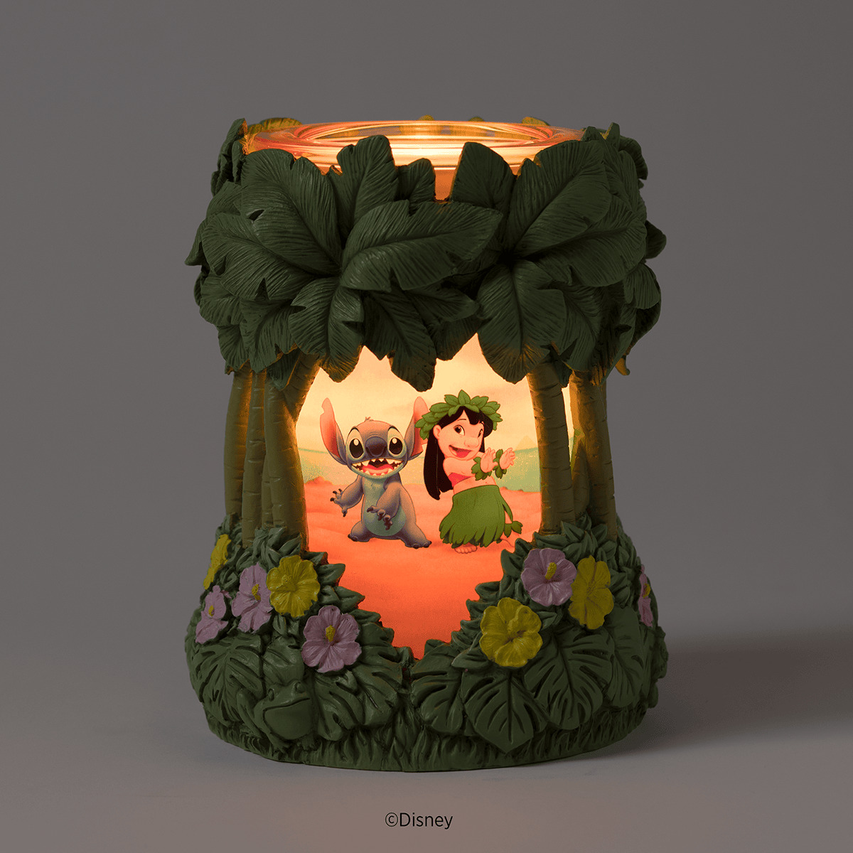 Cylindrical Scentsy Warmer with textured green leaves and flowers, illuminated scene of Lilo and Stitch in a tropical setting, warm orange glow at top