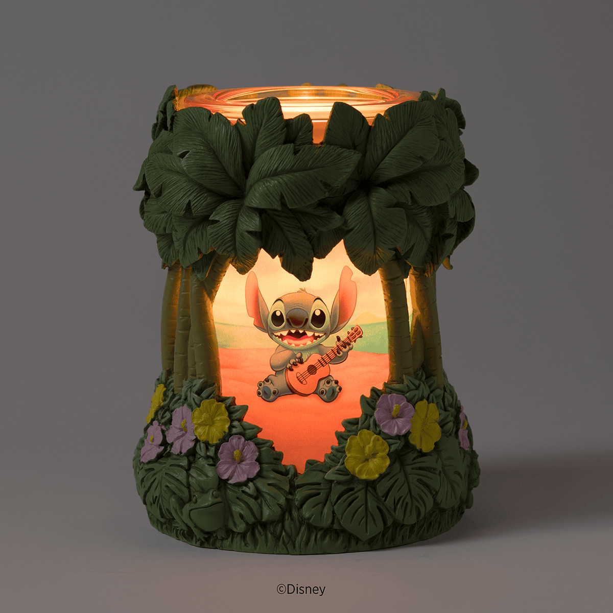 Illuminated Scentsy Warmer with green leafy canopy, purple and yellow flowers, and a glowing scene of Stitch playing ukulele in a tropical sunset setting