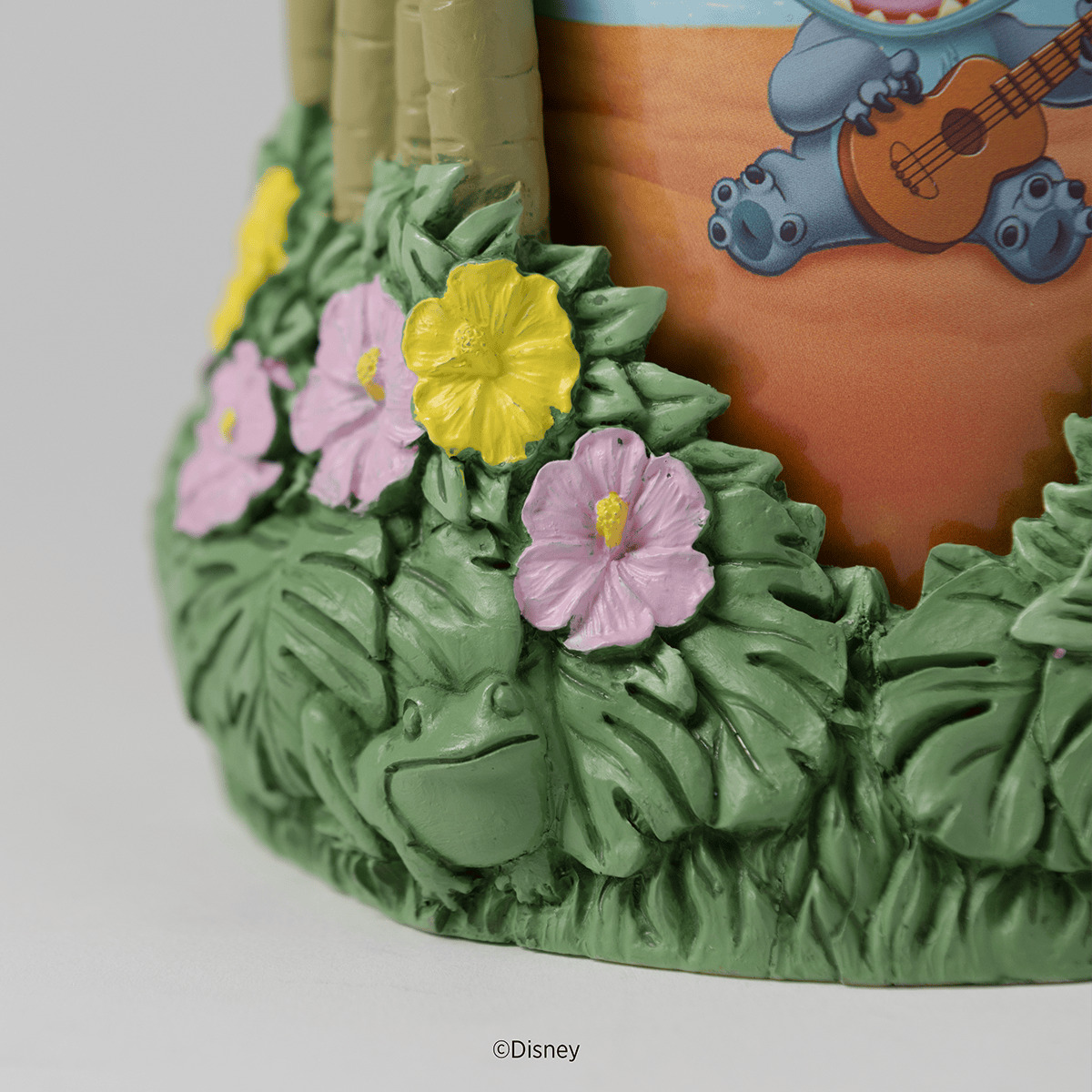Ceramic warmer with terracotta upper chamber featuring blue ukulele-playing characters, green leafy base adorned with yellow and pink flowers, the Disney Lilo & Stitch: Aloha-Ohana Scentsy Warmer