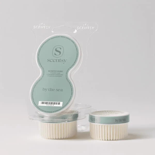 Two cream-coloured ridged Scentsy Pods with sage-green labels showing "by the sea" text, displayed alongside their clear blister packaging showing the By the Sea Scentsy Pods branding and product details