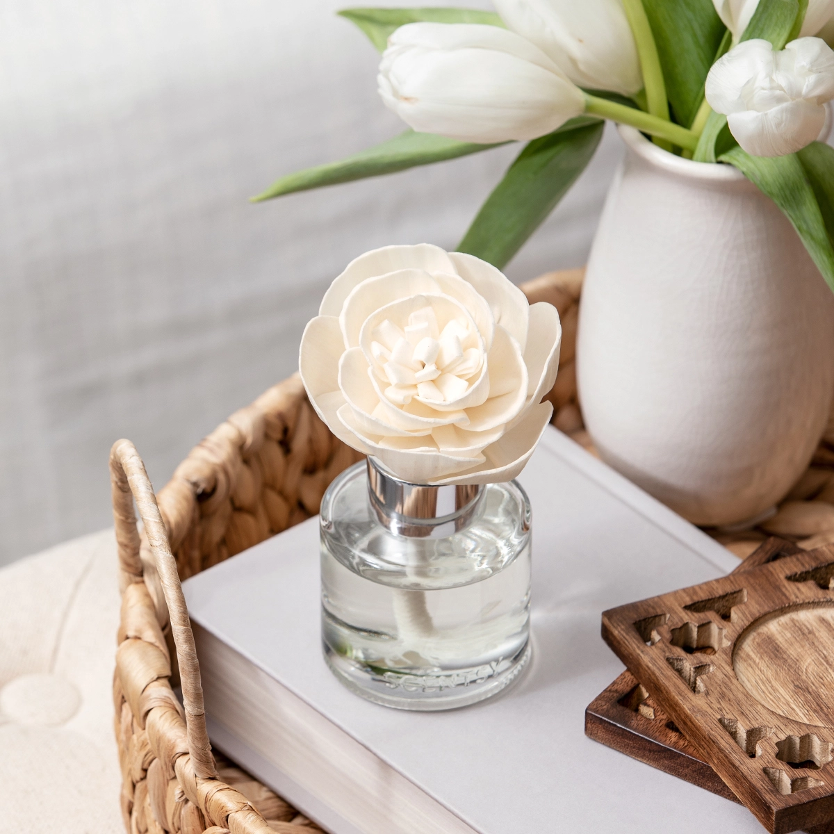 Cream rose-shaped Fragrance Flower in a clear glass bottle with metal collar, displayed on a white tray surrounded by white tulips and wooden accents, the Clothesline - Buttercup Belle Fragrance Flower