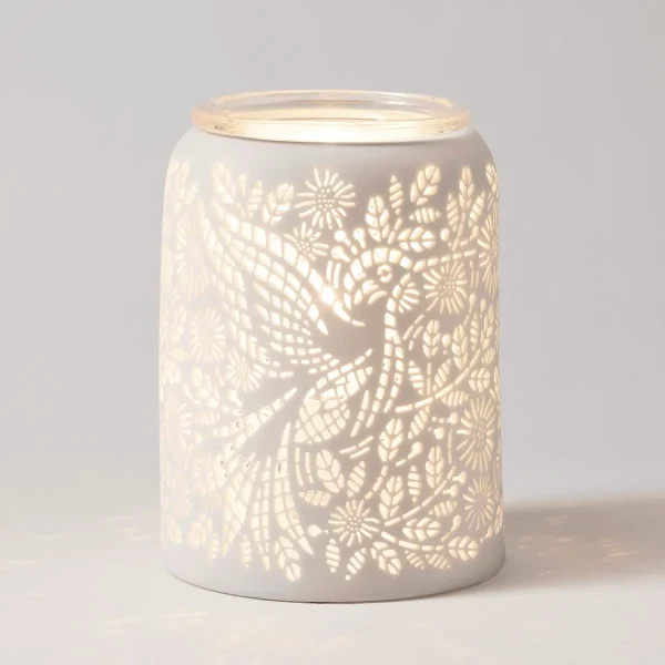 White ceramic cylindrical warmer with intricate cut-out pattern of hummingbirds, flowers, and leaves that glow warmly when lit, topped with a clear glass lid, the Etched Hummingbird Scentsy Warmer