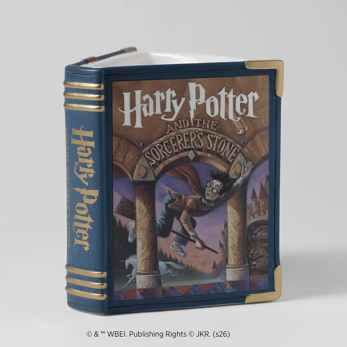 Navy blue decorative warmer shaped like a book with gold spine bands, a brown cover featuring Harry Potter and the Sorcerer's Stone artwork, and brass corner accents
