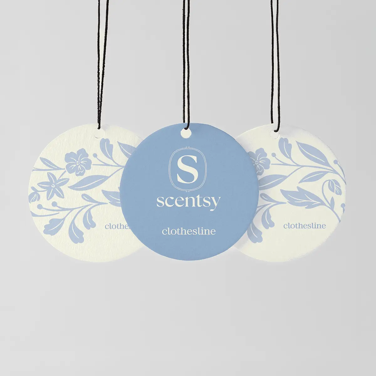 Three circular hanging fragrance discs with black strings, the centre one blue with the Scentsy logo, the two outer ones cream with blue floral patterns, labelled Clothesline Scent Circle 3-pack