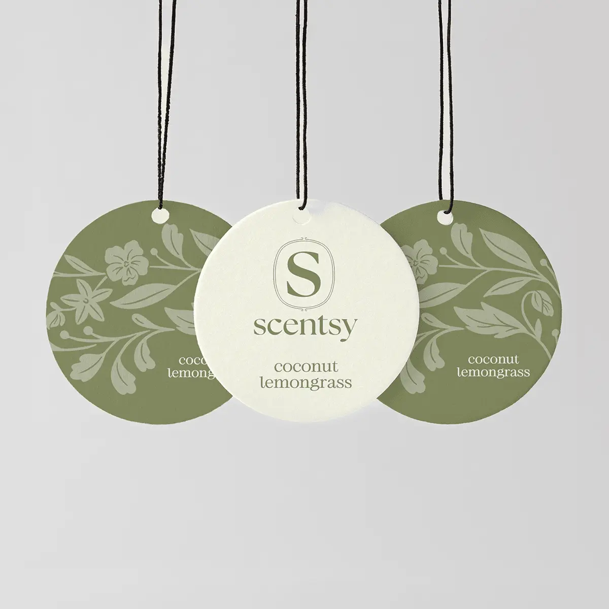 Three round Scent Circles hung from black strings—two sage-green with floral and leaf patterns, one cream with the Scentsy logo—the Coconut Lemongrass Scent Circle 3-pack