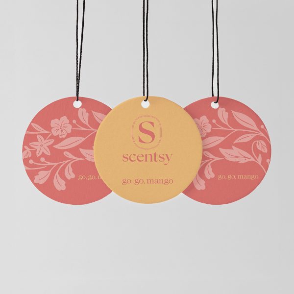 Three circular Scent Circles hanging from black strings with white beads: two coral-pink discs with floral and leaf patterns, and one golden-yellow disc with the Scentsy logo, for the Go, Go, Mango Scent Circle 3-pack