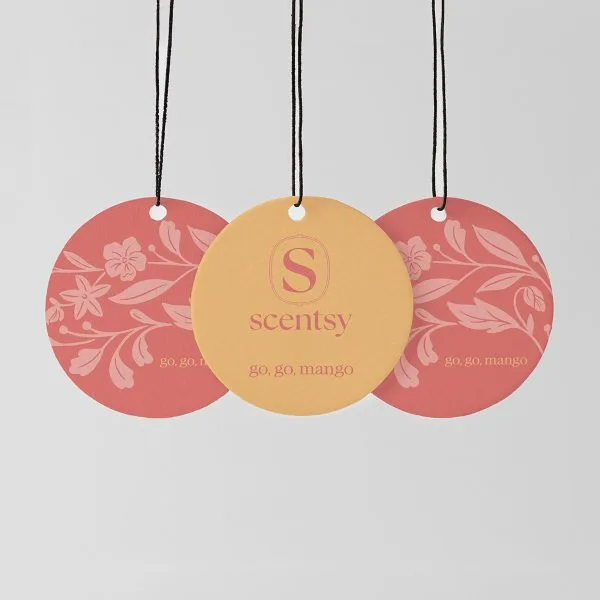 Three circular Scent Circles hanging from black strings with white beads: two coral-pink discs with floral and leaf patterns, and one golden-yellow disc with the Scentsy logo, for the Go, Go, Mango Scent Circle 3-pack