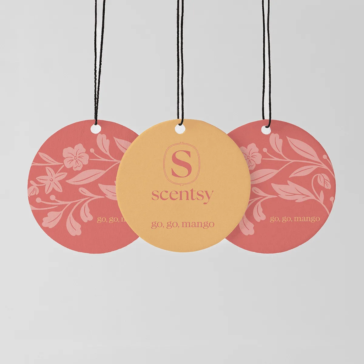 Three circular Scent Circles hanging from black strings with white beads: two coral-pink discs with floral and leaf patterns, and one golden-yellow disc with the Scentsy logo, for the Go, Go, Mango Scent Circle 3-pack