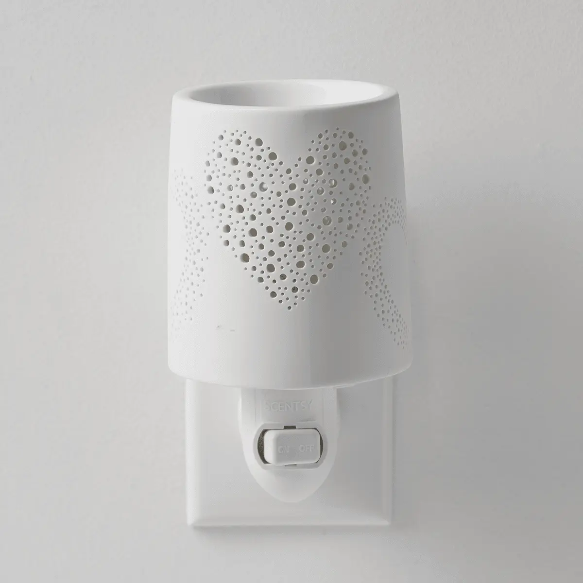 White ceramic mini warmer with a heart-shaped perforated design that casts light patterns, featuring a wall plug base