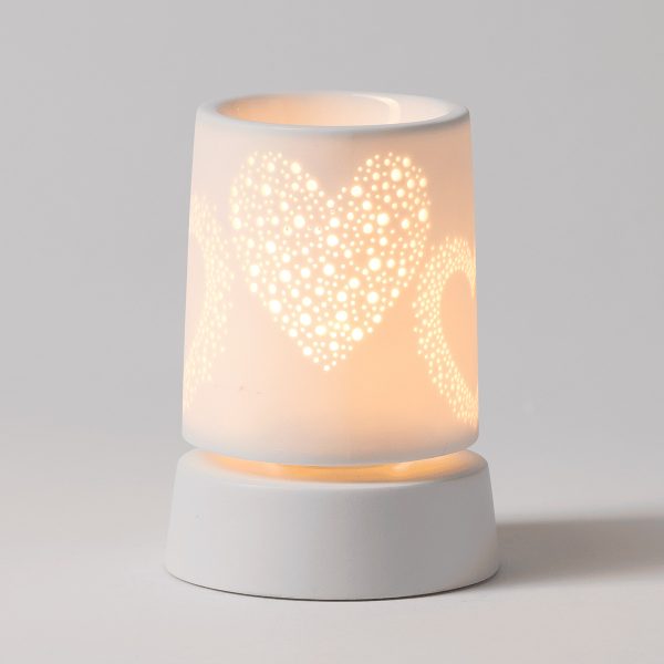 White ceramic mini warmer with perforated heart design that glows when lit, seated on a matching white cylindrical base, the Heart to Heart Mini Scentsy Warmer with Tabletop Base