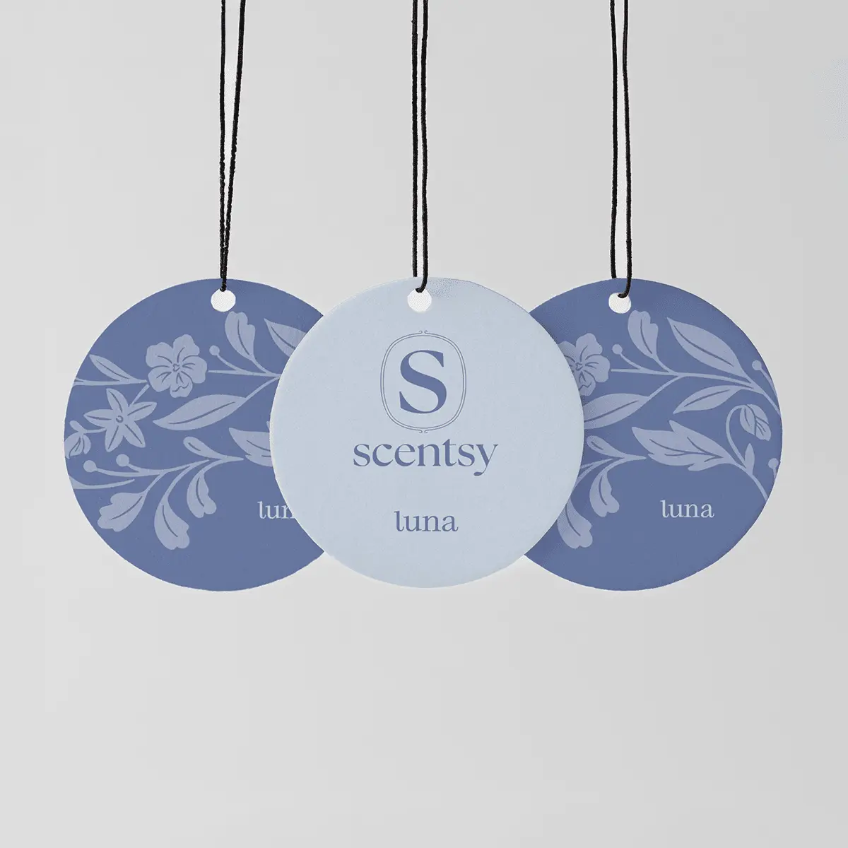 Three circular hanging fragrance tags with black cords: two in deep blue with floral leaf designs, one in pale blue with the Scentsy logo, all labelled luna, the Luna Scent Circle 3-pack