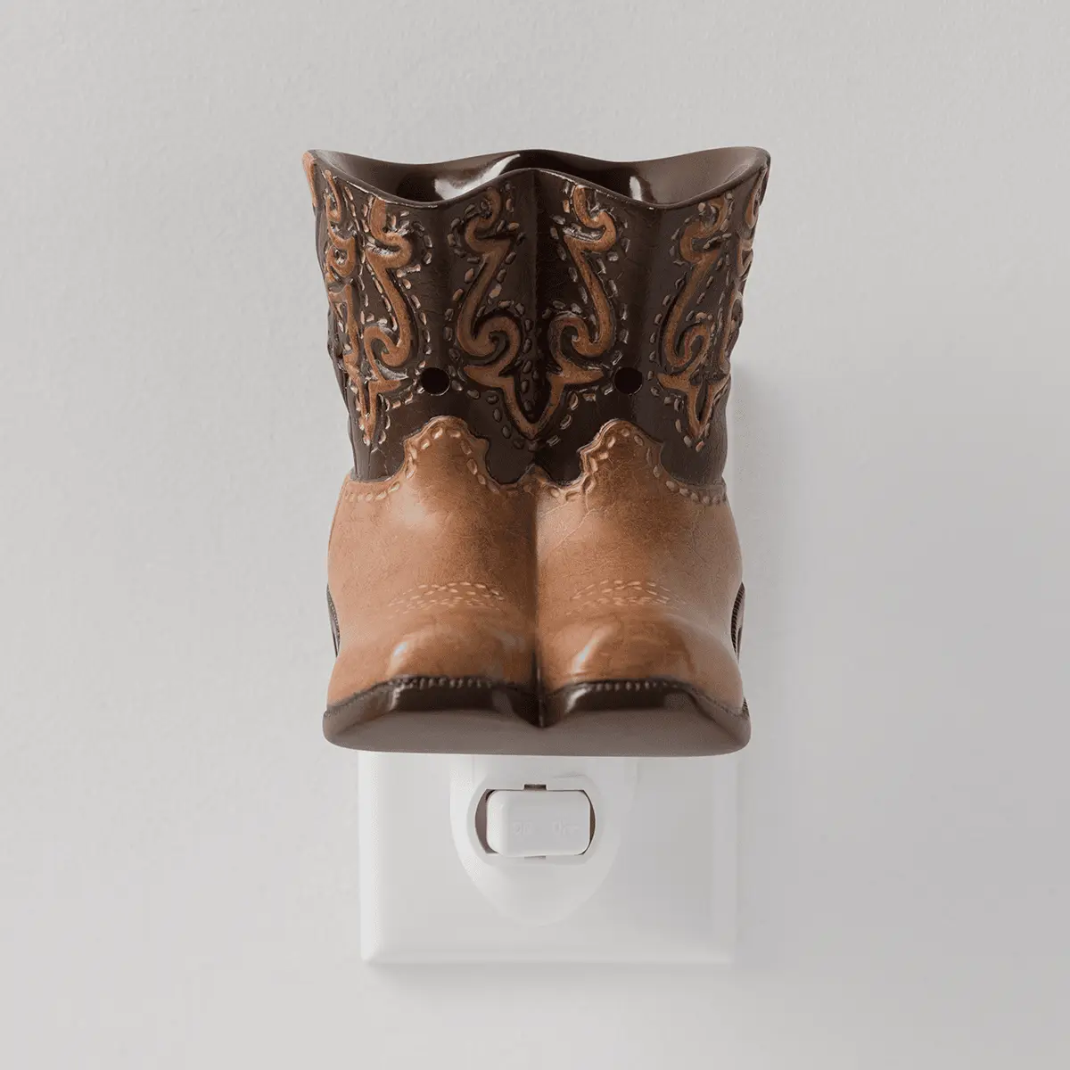 Cowboy boot-shaped ceramic warmer in tan and dark brown with ornate scrolled tooling detail, mounted on a white wall plug base, the Rodeo Mini Scentsy Warmer