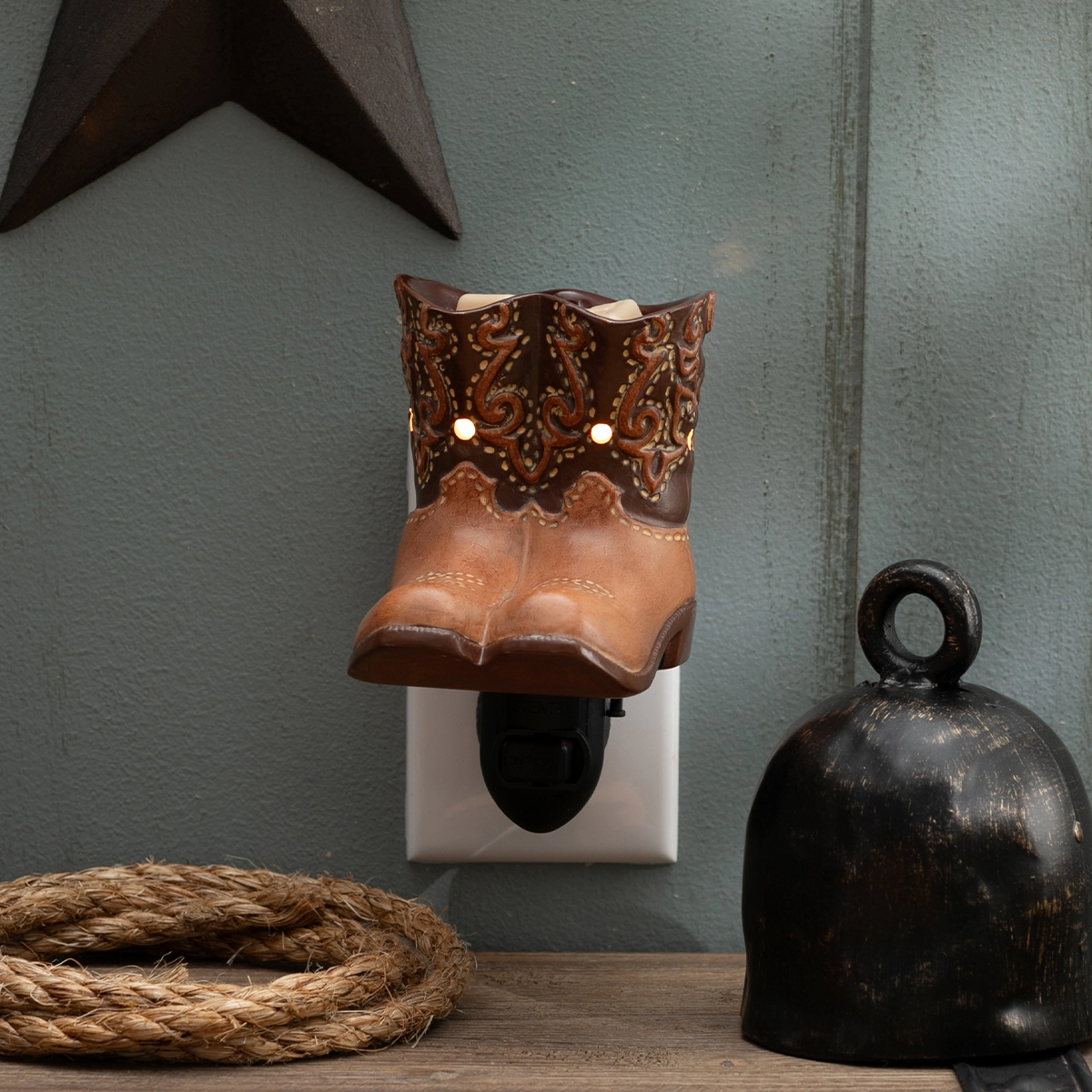 Brown leather cowboy boot-shaped mini warmer with ornate scrollwork cuff and perforated details, mounted on a white wall plug base