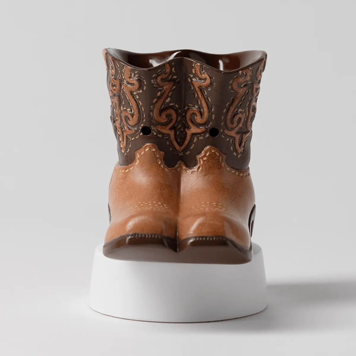 Cowboy boot-shaped mini warmer in brown and tan with ornate scrollwork detailing, seated on a white cylindrical base, the Rodeo Mini Scentsy Warmer with Tabletop Base