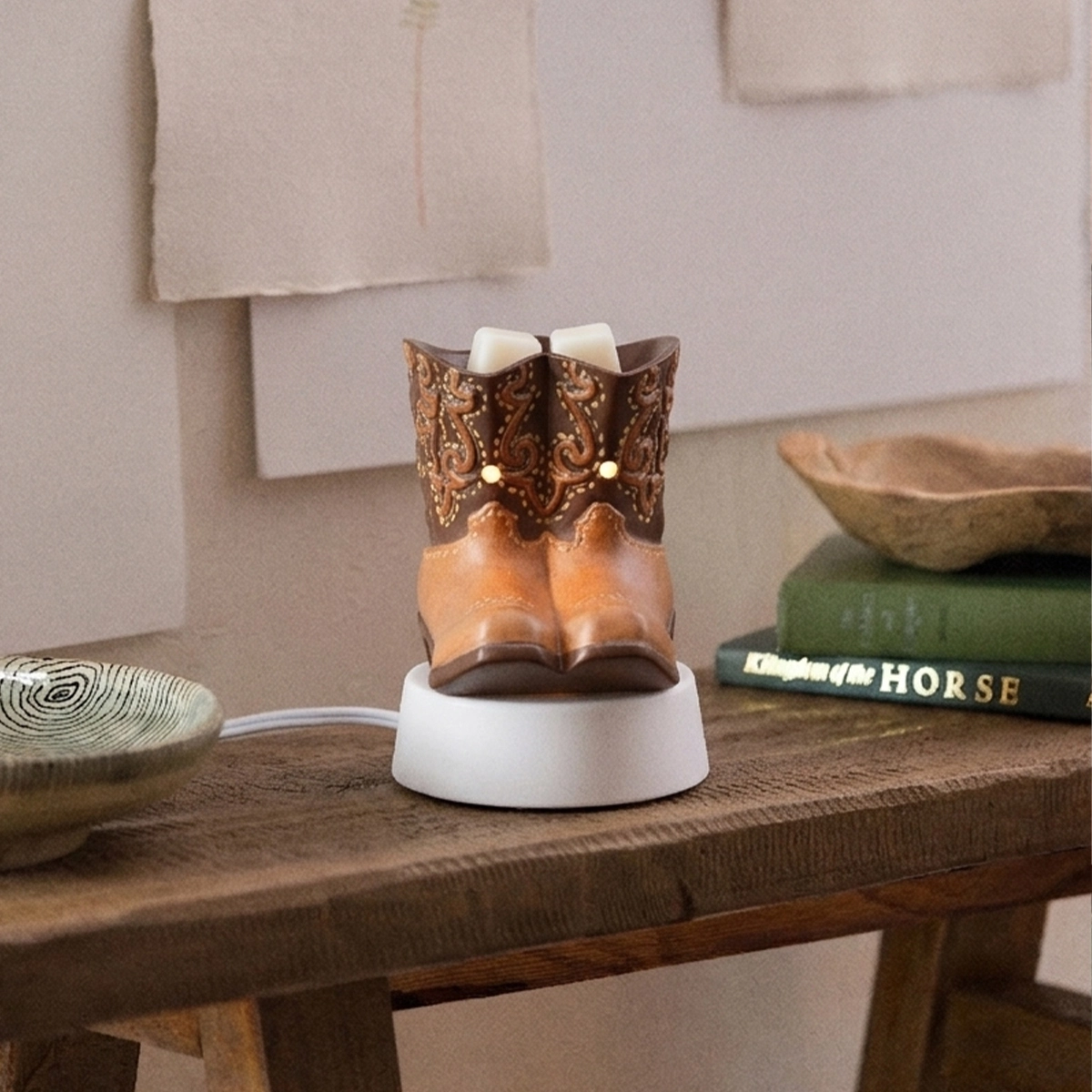 Brown leather cowboy boot-shaped mini warmer with ornate scrollwork cuff and white wax top, seated on a white round tabletop base