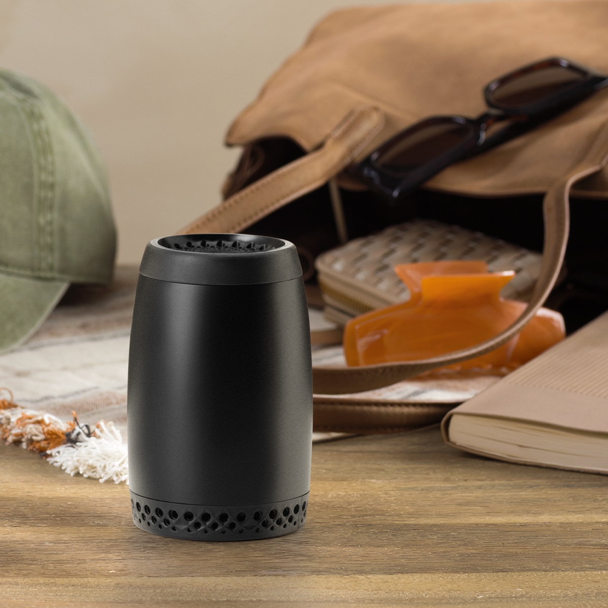 Compact black cylindrical diffuser with perforated base, displayed on wooden surface surrounded by travel accessories