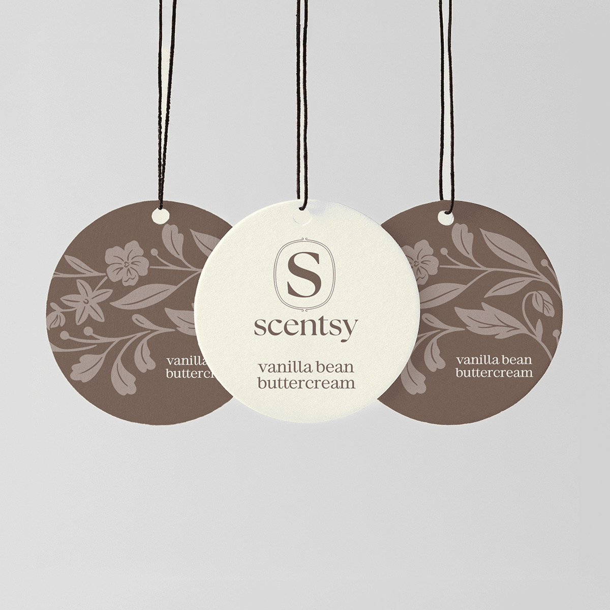 Three circular hanging Scent Circles with black cords and small white beads: cream centre disc with Scentsy logo and "vanilla bean buttercream" text, flanked by two taupe discs with floral damask pattern, for the Vanilla Bean Buttercream Scent Circle 3-pack