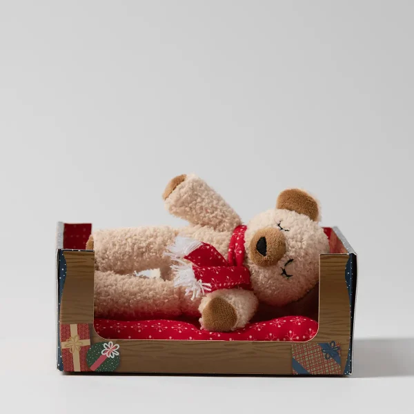 Cream curly plush bear with sleepy eyes and a red snowflake scarf lying on a red cushion in a wood-print box, the Cranberry the Bear Scentsy Beddy-Bye Buddy