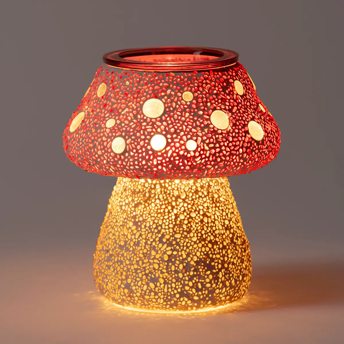 Mushroom-shaped ceramic warmer with a red spotted cap and golden stem, perforated with circular cutouts that glow when lit, the Cute as a Button Scentsy Warmer