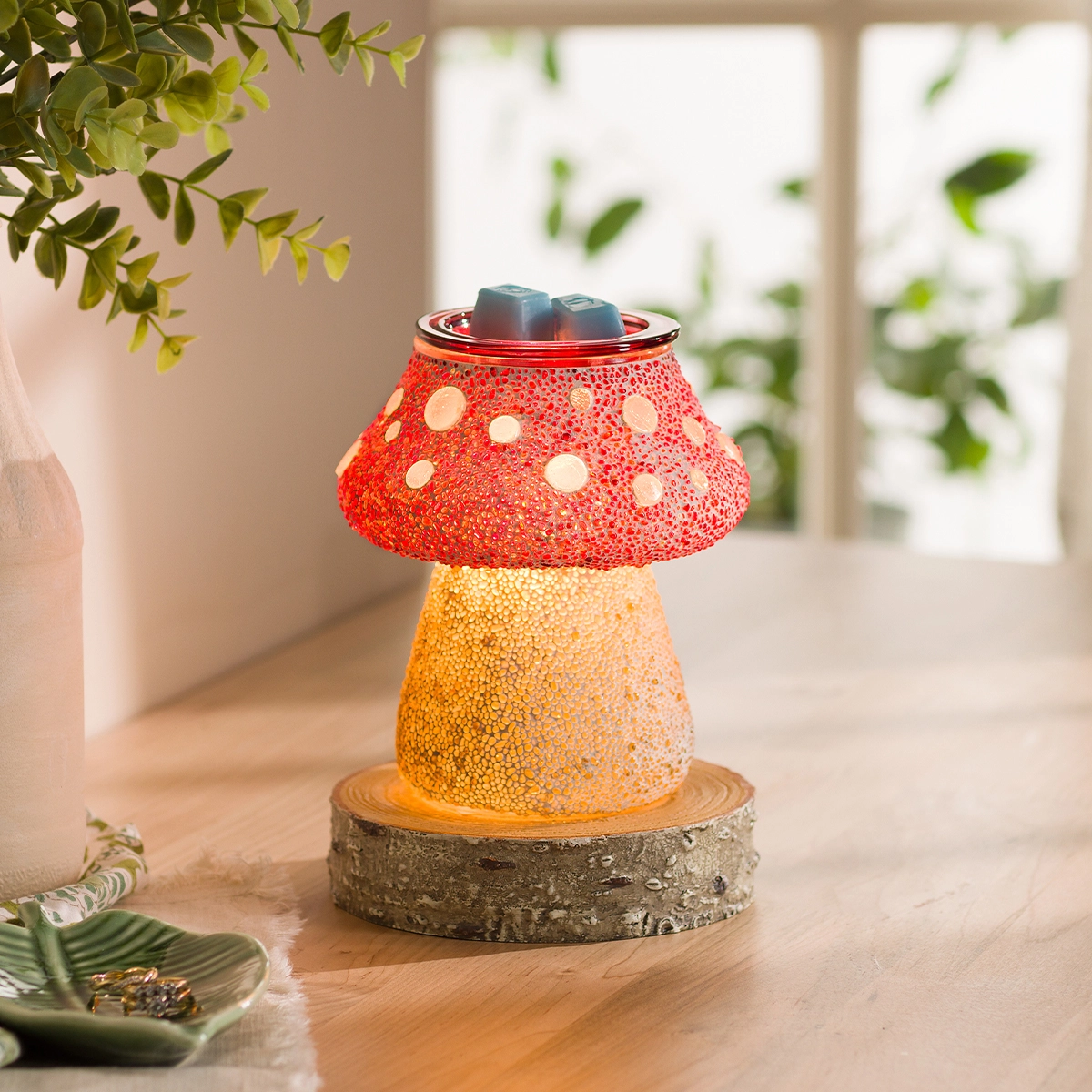 Mushroom-shaped warmer with a textured red cap dotted with cream spots, golden stem, and bark-textured base, topped with a chrome lid holding two wax cubes