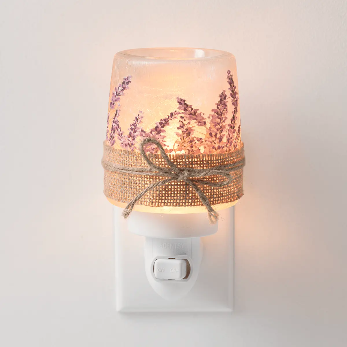 Frosted glass warmer with purple lavender sprigs and a gold mesh ribbon bow, illuminated from within, mounted on a white plug-in base, the Lavender Fields Mini Scentsy Warmer