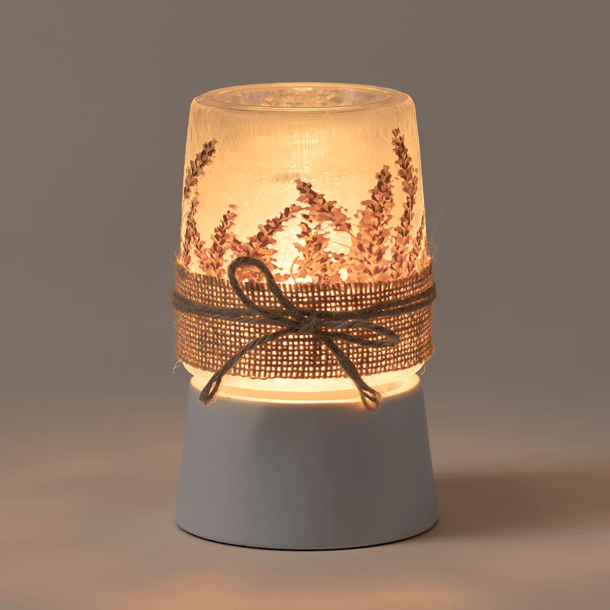 Lit mini warmer with frosted glass upper bowl printed with lavender sprigs, cream mesh ribbon band, and white ceramic tabletop base