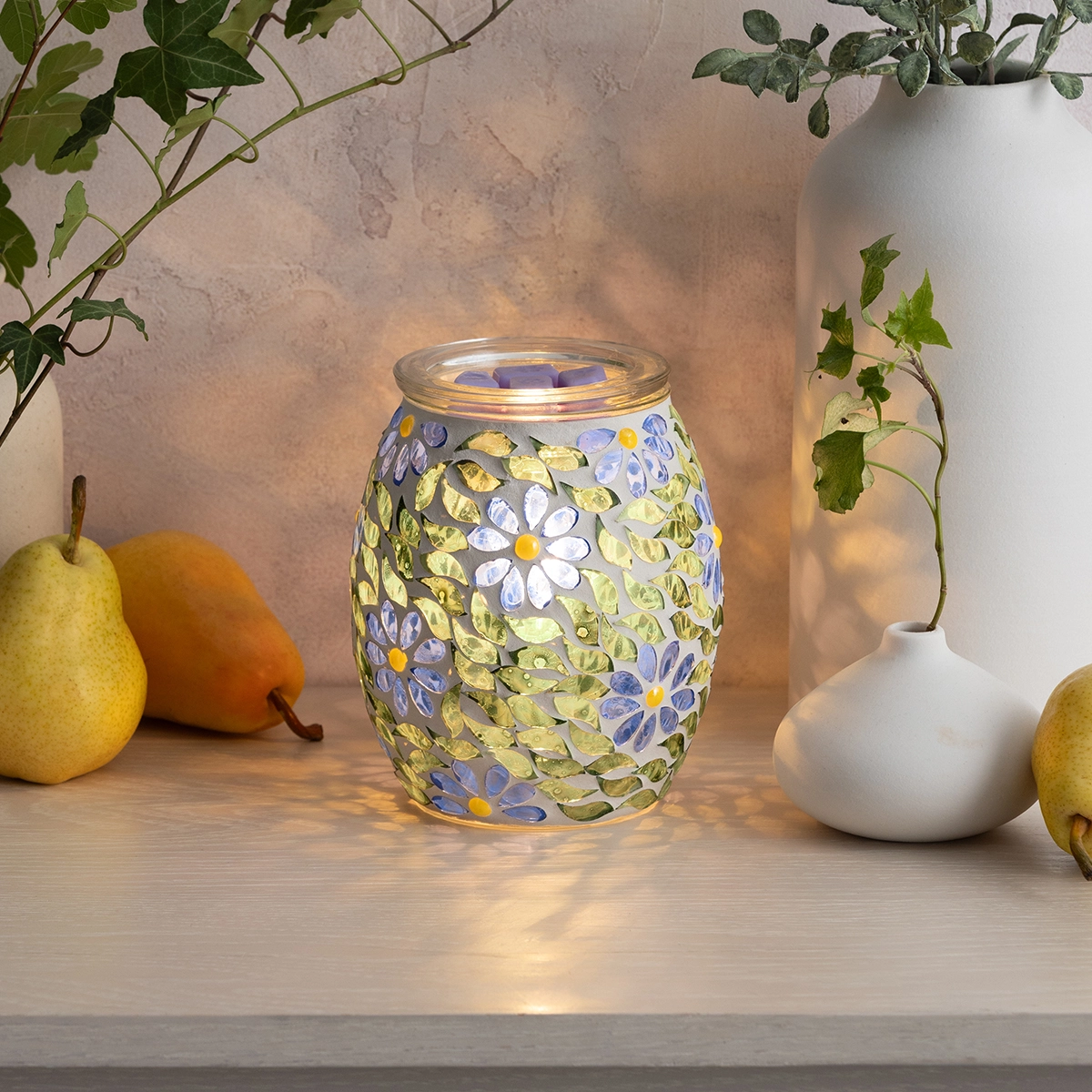 Glass warmer with purple and white daisies and leafy vines in yellow and green tones, lit from within, the Periwinkle Petals Scentsy Warmer