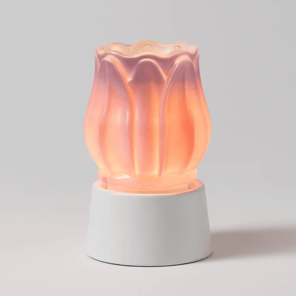 Translucent rose-pink warmer shaped like layered flower petals with warm orange-amber glow, sitting on a white ceramic cylindrical base, the Prismatic Petal Mini Scentsy Warmer with Tabletop Base