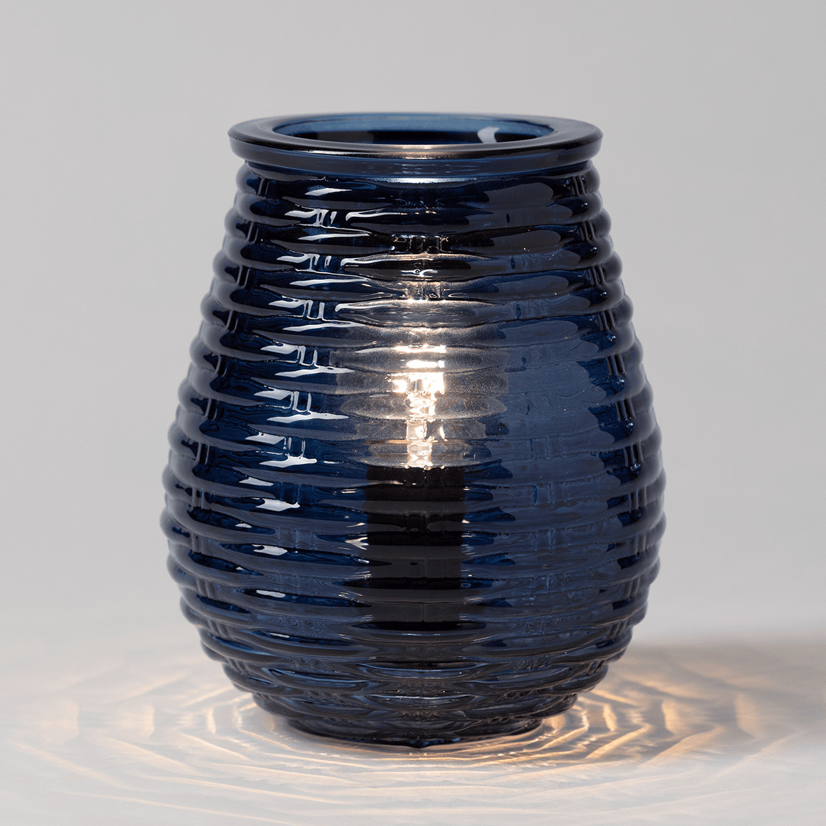 Deep blue glossy ceramic warmer with a rippled horizontal texture pattern, the Azure Ripples Scentsy Warmer, casting warm light through the ridged surface