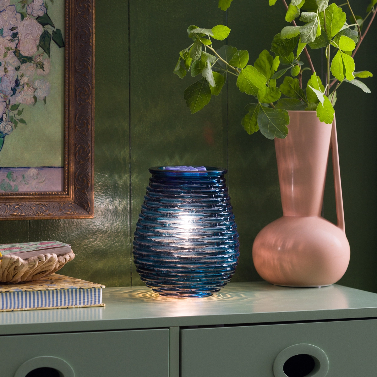 Deep blue glass warmer with horizontal rippled texture that refracts light, the Azure Ripples Scentsy Warmer, displayed on a green cabinet beside a pink vase