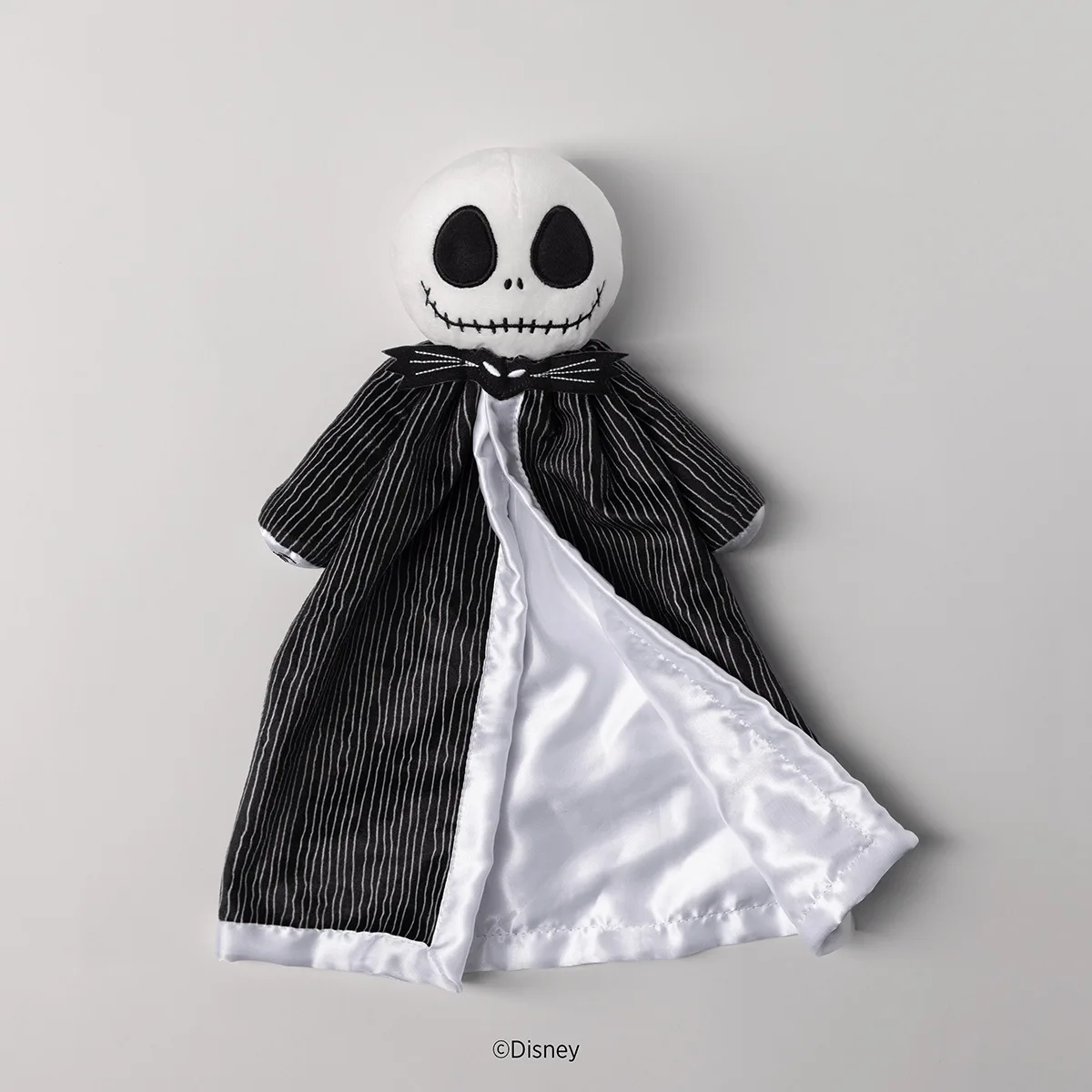 Soft plush toy with a white round head featuring large black oval eyes and a stitched smile, wearing a black pinstriped jacket with a white silk-lined cape, the Disney Jack Skellington Scentsy Blankie Buddy