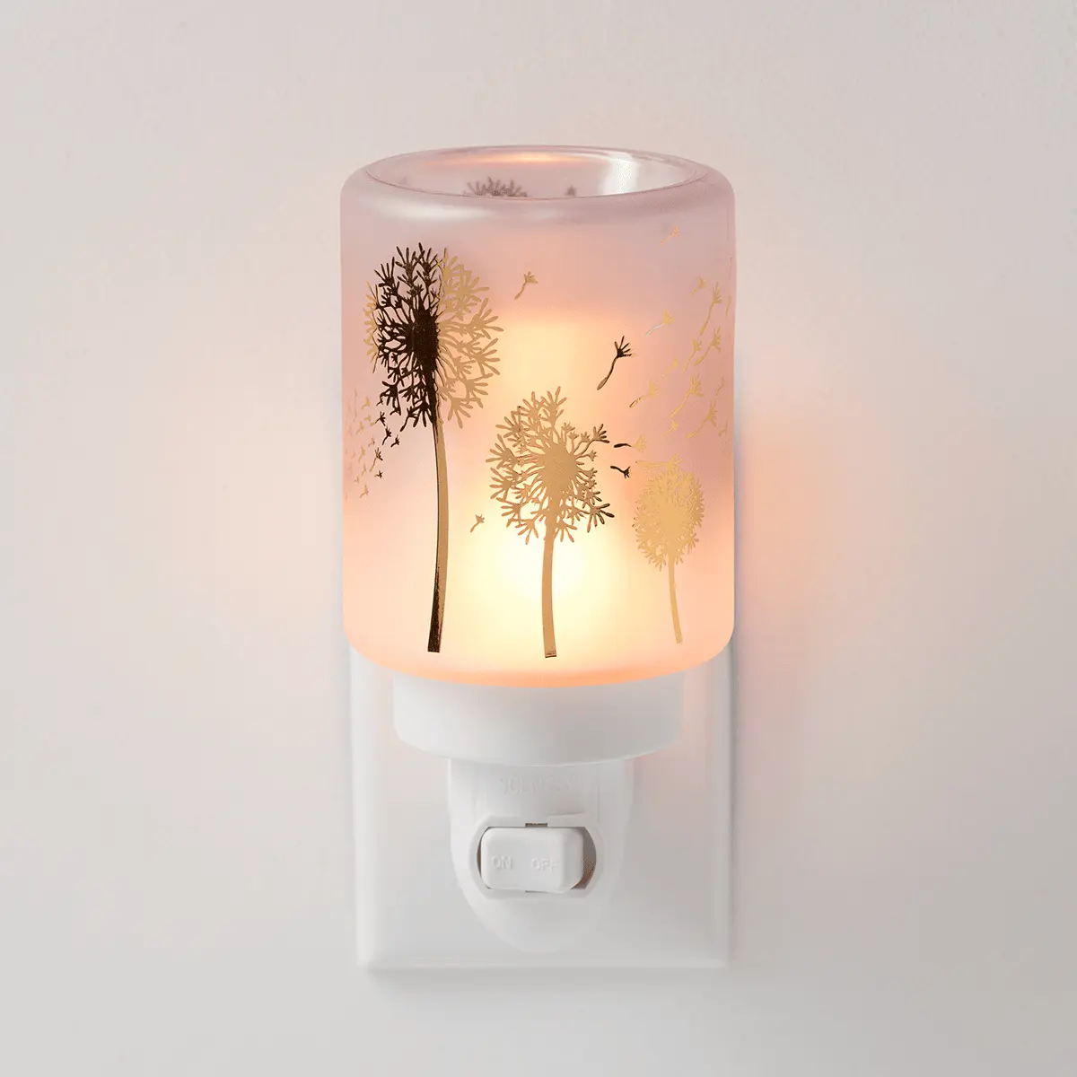 Frosted glass wall-plug warmer with dandelion silhouettes and flying seeds in warm gold and brown tones, glowing warm amber when lit, the Wishbloom Mini Scentsy Warmer