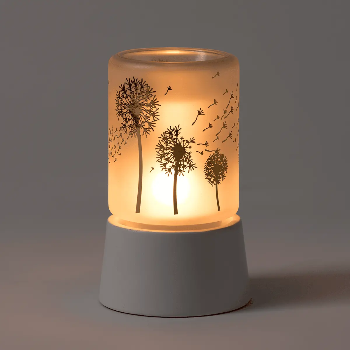 Cream and translucent ceramic mini warmer with etched dandelion design, illuminated from within, mounted on a white ceramic base, the Wishbloom Mini Scentsy Warmer with Tabletop Base