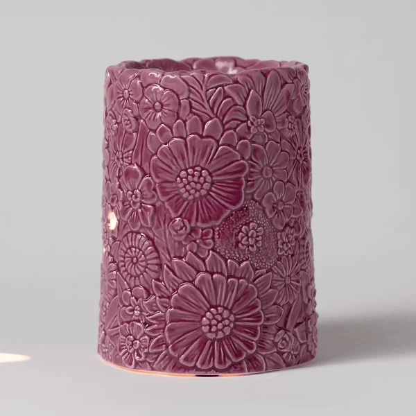 Cylindrical ceramic warmer in mauve pink with an all-over relief design of daisies and smaller flowers, the Dusky Petals Scentsy Warmer, with a warm glow visible at the base
