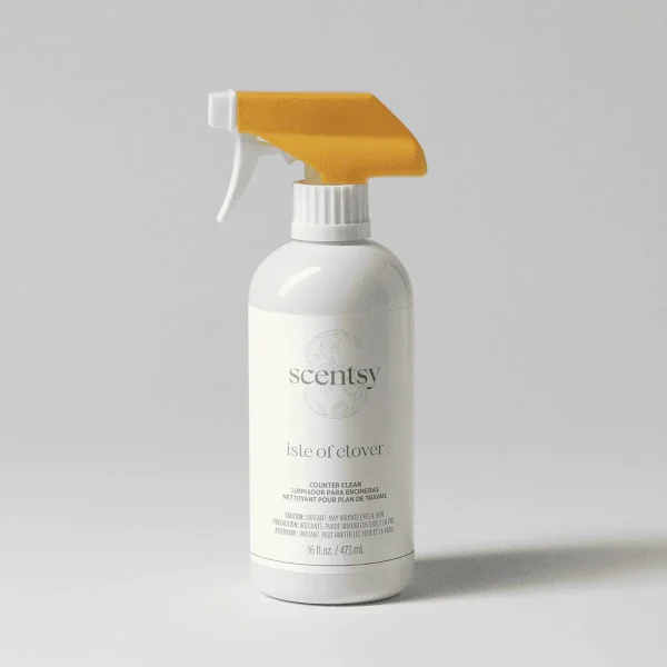 White spray bottle with gold trigger and cap, labeled Scentsy Isle of Clover Counter Clean, 473 mL, against a neutral background