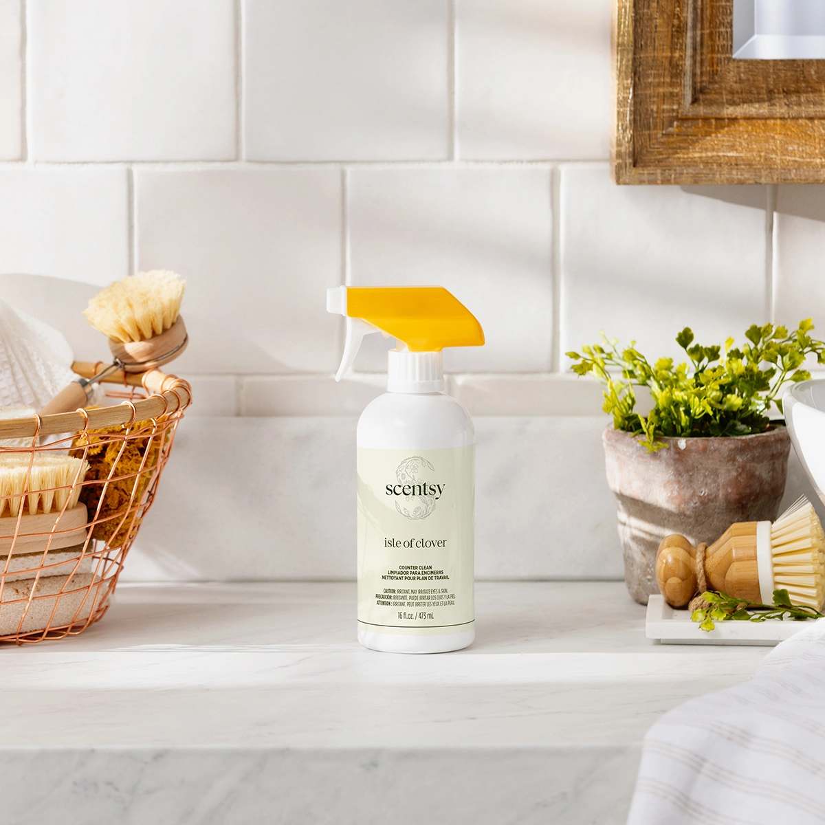 White spray bottle with yellow trigger and Scentsy branding, Isle of Clover Counter Clean, displayed on a marble countertop with a white subway tile backsplash