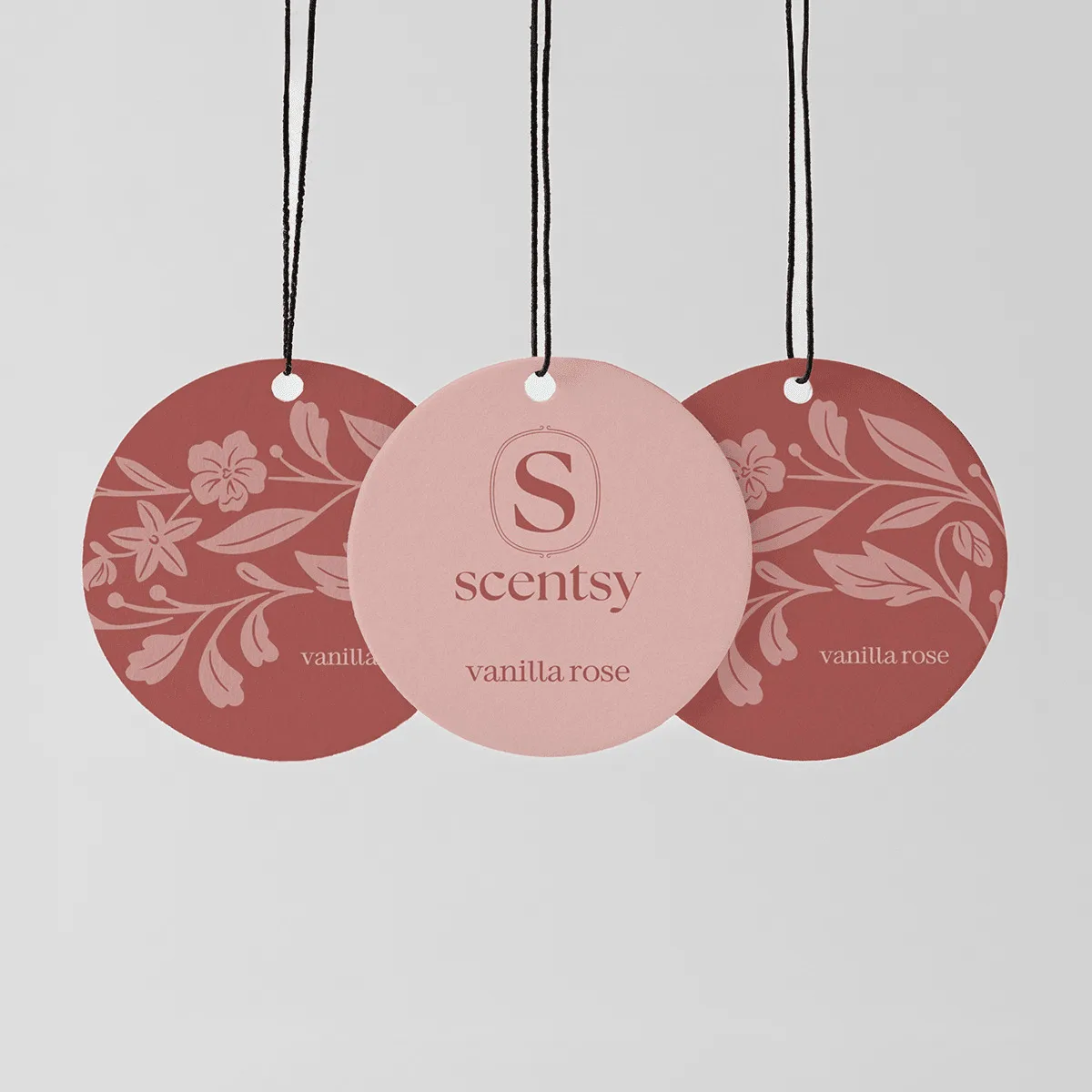 Three circular Scent Circles with black strings, in dusty rose and terracotta tones featuring floral and leaf patterns, the centre circle in pale pink with embossed Scentsy logo, the Vanilla Rose Scent Circle 3-pack