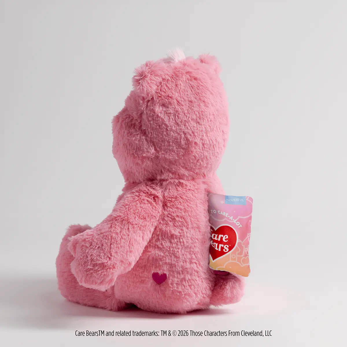 Pink fluffy plush bear sitting with a small heart symbol on its chest, wearing a Care Bears product tag