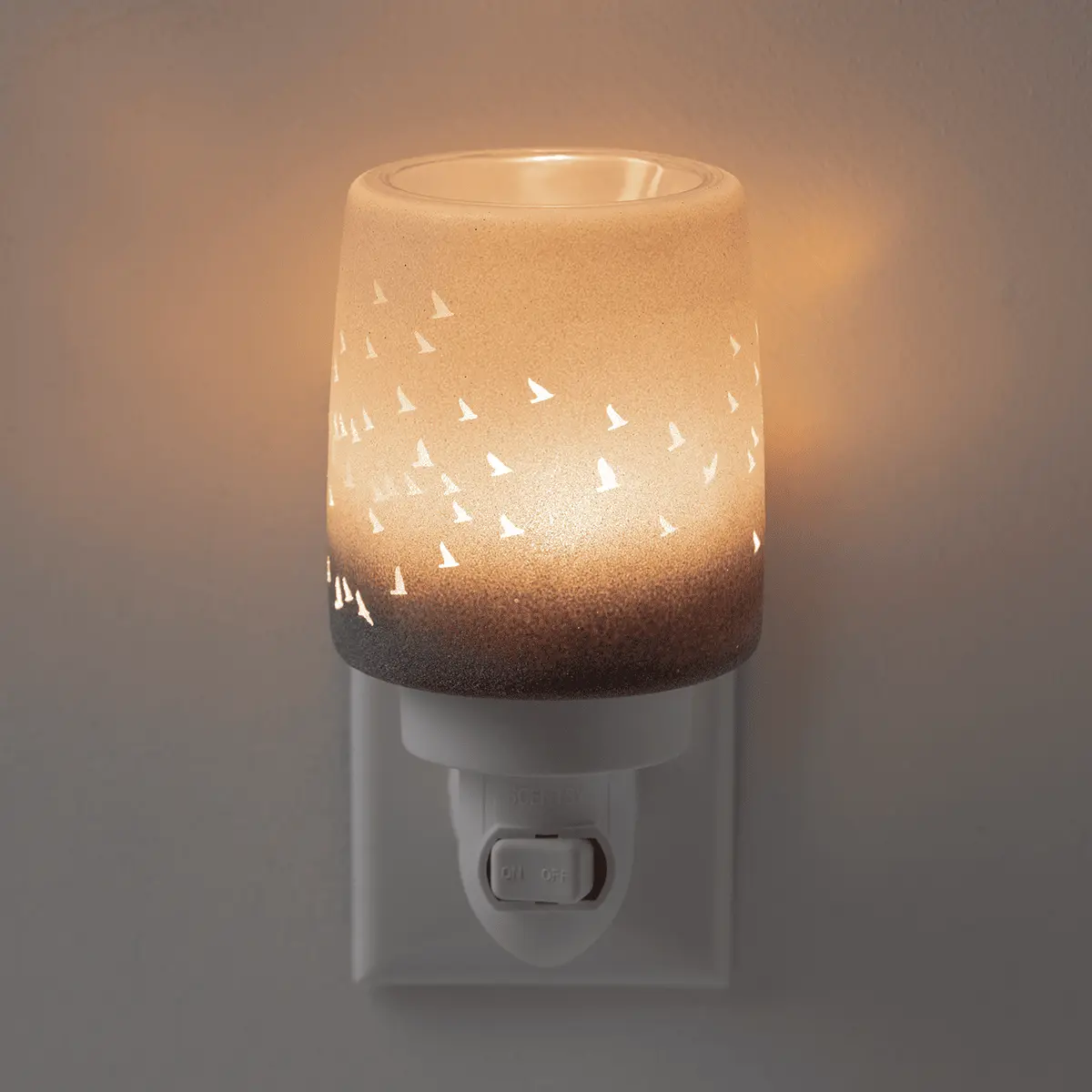Cylindrical ceramic mini warmer with ombré grey-to-cream glaze and sailboat cutout pattern, glowing when lit, the Waves & Wings Mini Scentsy Warmer