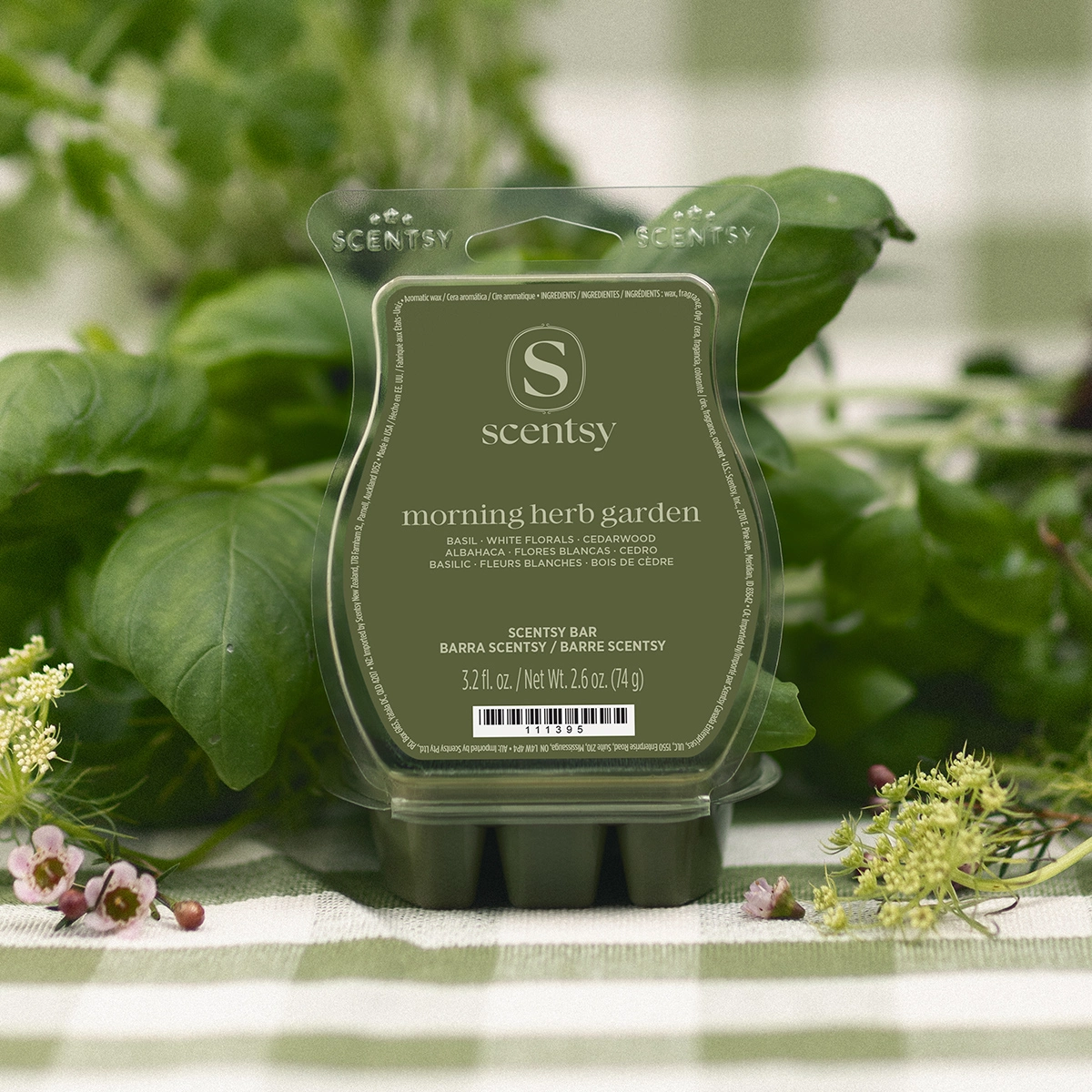 Translucent sage-green Scentsy wax bar moulded in a rounded shape with dual handle cutouts, labelled Morning Herb Garden, surrounded by fresh green foliage and delicate flowers