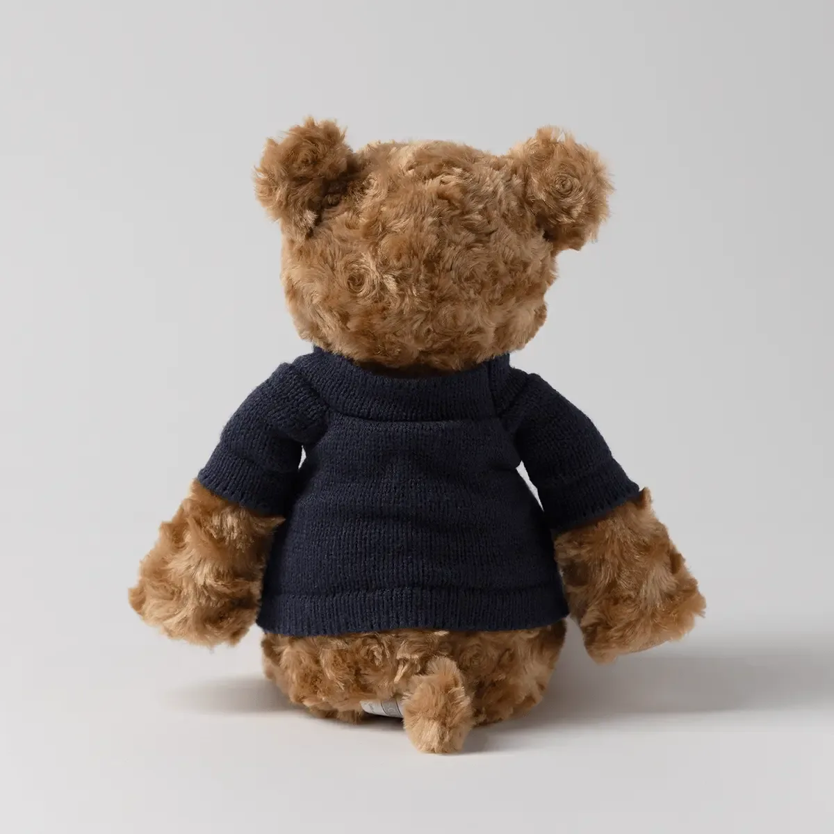 Tan curly plush bear with round ears wearing a navy knit sweater